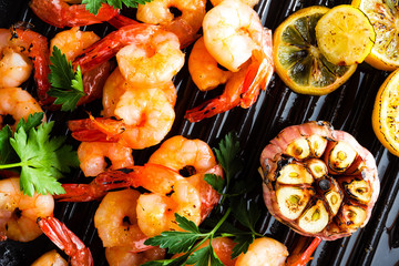 Prawns roasted on grill frying pan with lemon and garlic. Grilled shrimps, prawns. Seafood. Top view. Dark background