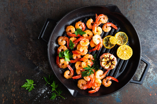 Prawns roasted on grill frying pan with lemon and garlic. Grilled shrimps, prawns. Seafood. Top view. Dark background