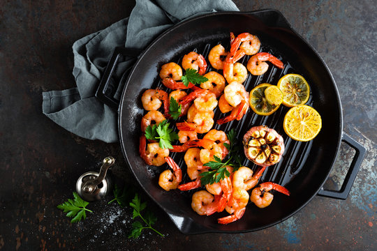 Prawns roasted on grill frying pan with lemon and garlic. Grilled shrimps, prawns. Seafood. Top view. Dark background