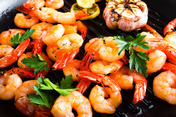 Prawns roasted on grill frying pan with lemon and garlic. Grilled shrimps, prawns. Seafood. Closeup. Dark background