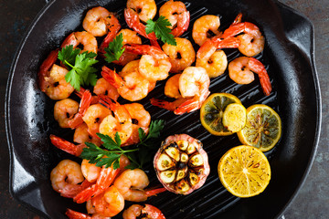 Prawns roasted on grill frying pan with lemon and garlic. Grilled shrimps, prawns. Seafood. Top view. Dark background