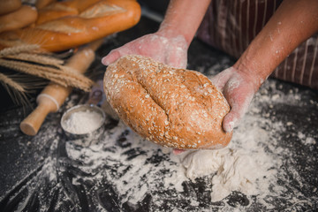 Man preparing buns at table in bakery, Man sprinkling flour over fresh dough on kitchen table