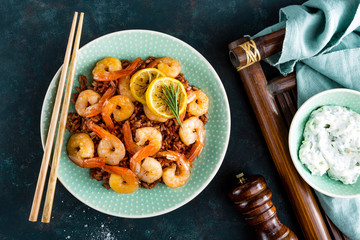 Prawns roasted on grill and boiled brown rice on plate. Grilled shrimps, prawns with rice. Seafood. Asian cuisine. Top view. Dark background