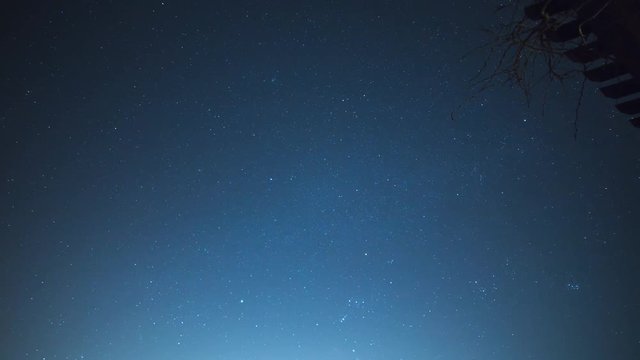 Night sky time lapse with stars and light clouds overhead.