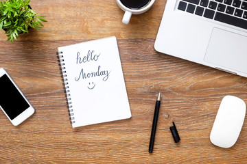 Notebook with hello Monday text on it over wood office desk table with supplies. Top view, flat lay.