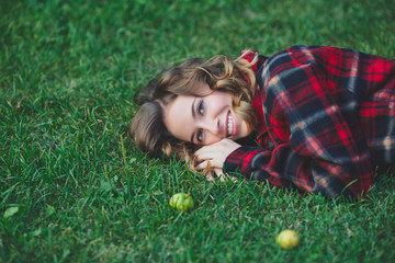 Beautiful young woman in a male flannel shirt lying on green grass. Outdoor portrait in city park