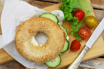 White sesame bagel with cream cheese and cucumber, cherry tomatoes on wooden board

