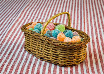 Fototapeta na wymiar Sugar coated jelly sweets in wicker basket on striped tablecloth