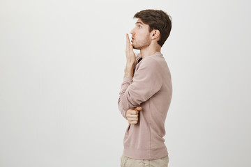 Profile portrait of handsome young man covering mouth with hand as if seeing something...