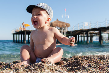 A small child in a cap playing small pebbles (sand) on the beach, emotionally laughing