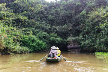 Rowing woman row a boat with tourist on the river with cave entrance in the background at Trang An Grottoes in Ninh Binh, Vietnam.
