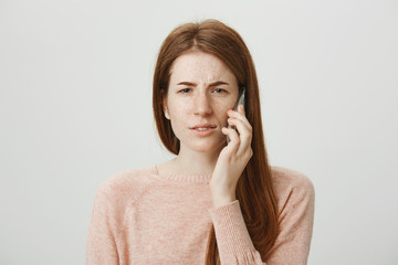 Close-up portrait of cute caucasian redhead girl talking on smartphone and expressing disbelief,...