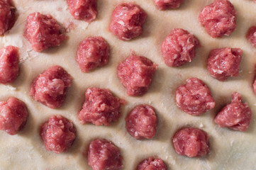 Meat balls laying on the rolled out wheat dough. Potstickers cooking.