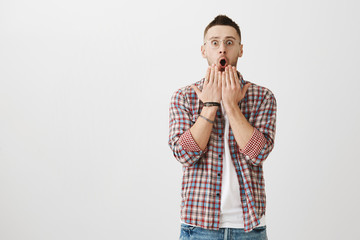 Shocked and terrified handsome male with bristle and transparent glasses holding hands above opened mouth and staring at camera, being surprised. Guy witnessed how girlfriend woke up from coma