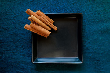 Pile Dried Cinnamon Sticks Placed on Black Plate Which Placed on Blue Stone Surface Background