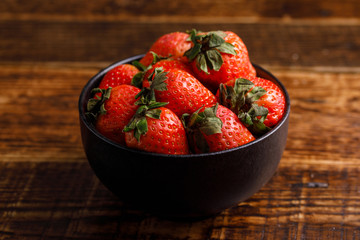 Ripe strawberries in a black cup on a wooden table. Strawberry in a cup closeup