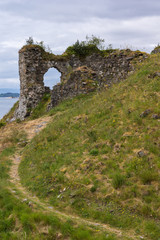 Fototapeta na wymiar Stromeferry, Scotland - June 10, 2012: Path leading up green hill to Window in rock wall of Castle Strome ruins at Loch Carron. Mountains on horizon.