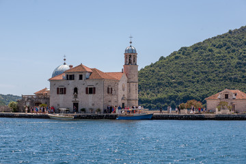 Fototapeta na wymiar Fjord in Adriatic Sea. Our Lady of the Rock island and Church in Perast on shore of Boka Kotor bay (Boka Kotorska), Montenegro, Europe.