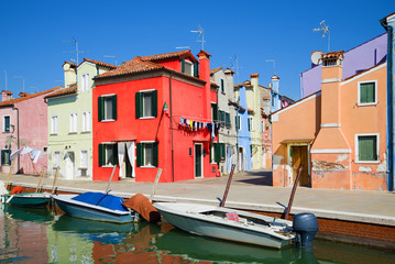 Fototapeta na wymiar Red house on the embankment of the city channel. Sunny day on the Burano island, Venice