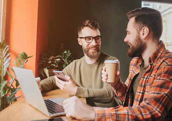 Cut view of guys sitting and having a conversation. On of them is dranking coffee while another is explaining something to him and holding a phone.