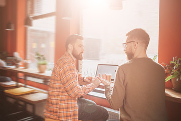 Fototapeta premium A view where two best friends are sitting at the table and having conversation. They are in cafe in a beautiful sunny day.