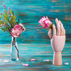 Rose in wooden hand on turquoise background