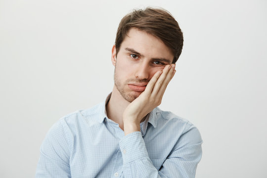 Indoor shot of upset irritated caucasian guy leaning on palm and sighing at camera, being bored and fed up of annoying meeting in office, wanting to go home, tired of wasting time over gray wall