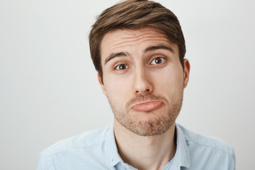 Obraz premium Close-up portrait of pity cute caucasian guy making angel face and sulking, feeling blame and trying to make innocent expression, standing over gray background, convincing he is not guilty