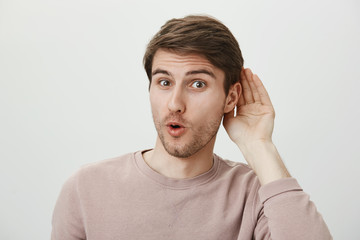 Guy enjoys put hit nose in business of other people. Thrilled handsome male holding palm near ear and saying wow, overhearing conversation and wanting to spread rumor, standing over gray wall