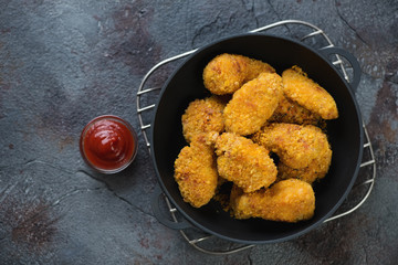 Top view of fried chicken wings with breading and sauce in a cast-iron pan, horizontal shot on a weathered asphalt background