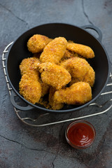 Cast-iron pan with fried breaded chicken wings on a metal cooling rack, cracked weathered asphalt background, vertical shot