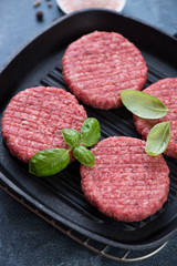 Cast-iron grill with raw burgers made of marbled beef meat, vertical shot, close-up, selective focus