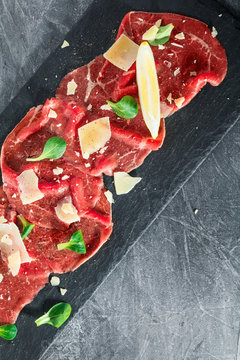 Top view of the raw beef carpaccio with parmesan cheese on a black shale service board. Delicatessen food. Copy space.