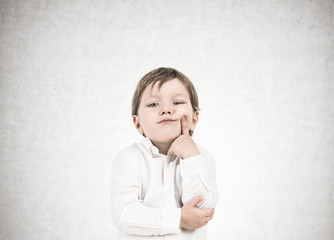 Thinking little boy, finger on cheek, concrete