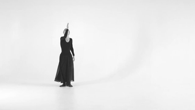 Black and white image. Young woman choreographer dancing in a black suit against a white wall background. Modern dance 4k