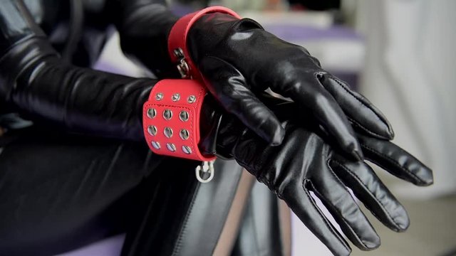 Woman in black outfit with red cuffs close-up. Female hands in leather gloves and handcuffs.