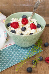 Cottage cheese in bowl with raspberries and blueberries on wooden background. Healthy breakfast .Place under the text