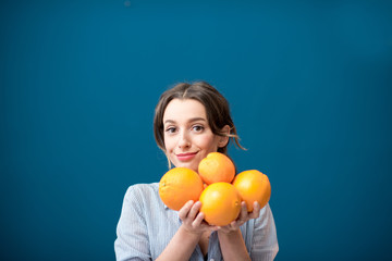 Portrait of a young and happy woman with oranges on the blue wall background