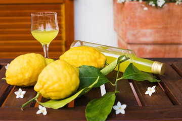 Lemonade or limoncello in a glass bottle, glass, lemons with leaves on a serving table on the...