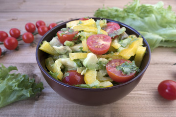 Appetizing vegetable salad consisting of tomatoes, avocado, yellow sweet pepper, lettuce leaves.
