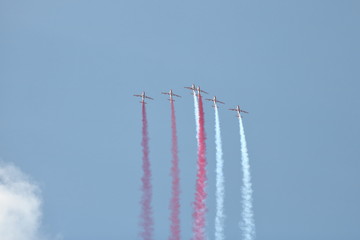Grupa samolotów akrobacyjnych w powietrzu, leci ostro do góry zostawiając za każdym z nich biały i czerwony dym, niebieskie niebo - obrazy, fototapety, plakaty