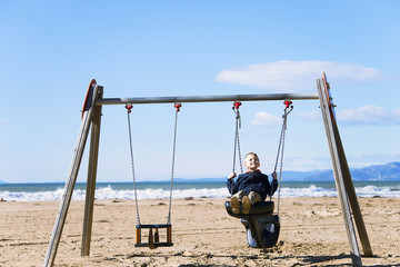  boy is riding a wooden swing on the beach