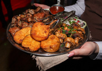 dish with potatoes and barbecue in the hands of the waiter