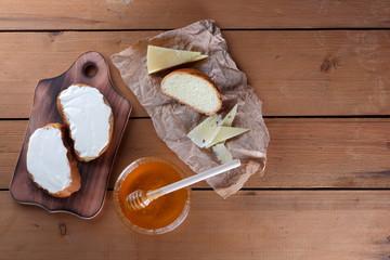 Cheese on a wooden board, food on parchment paper, sandwiches with soft cheese, honey in glass dishes, copy space, cheese pattern, wood background, wooden cutlery, simple food, art