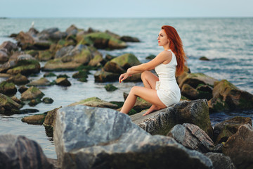 Fototapeta na wymiar Young pretty woman sitting lonely on rocks at sea