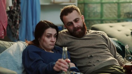 Sad alcoholic man and woman with a beer sit on sofa talk in home drinker alcohol drunk beverage male belly addiction adult alcoholism alone problem portrait abuse depression stress cheers slow motion
