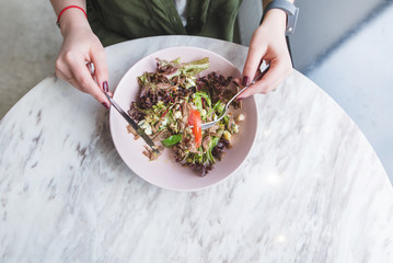 Hands of a woman and a plate of salad. A girl eating a salad in a light restaurant at the table overlooks the top. Good food at the restaurant