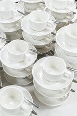 Sets of clean white cups and saucers in rows and one on another