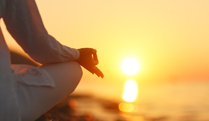 hands of woman meditating in yoga pose at sunset on beach