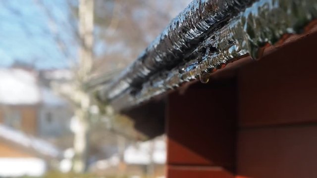 Snow smeling off from rooftop at spring, in bright sunlight and clear blue sky